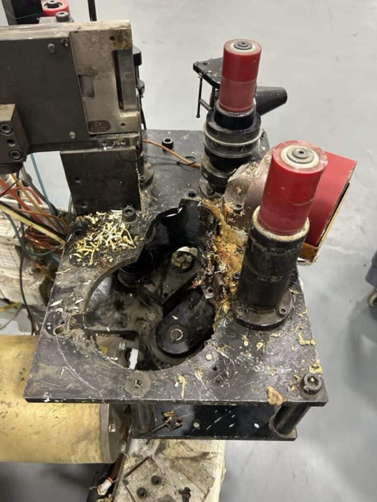 Corroded industrial machine component with damaged rollers and electrical wiring, showing signs of wear and debris.