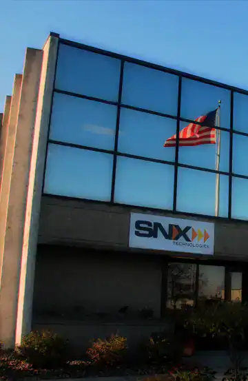 Bright modern office building with SNX Technologies signage and American flag reflecting on glass windows.